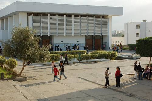 Edificio de fachada blanca con brise-soleil en el campus de la Universidad de Túnez El Manar, con estudiantes cruzando la explanada exterior