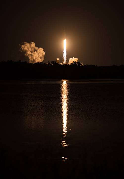 El despegue nocturno de un cohete Falcon Heavy reflejado sobre el agua