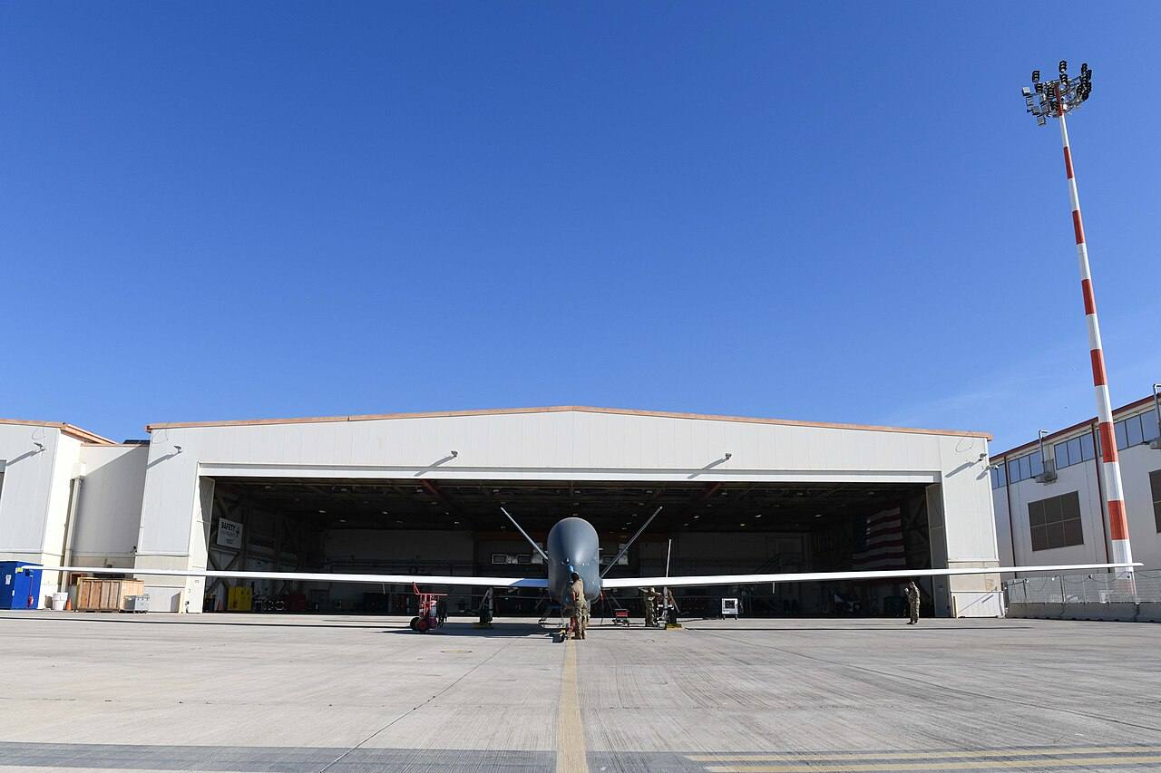 Dron militar de reconocimiento RQ-4 Global Hawk de EE. UU. en pista tras aterrizar, con personal de mantenimiento junto a él en la base de Sigonella, Italia