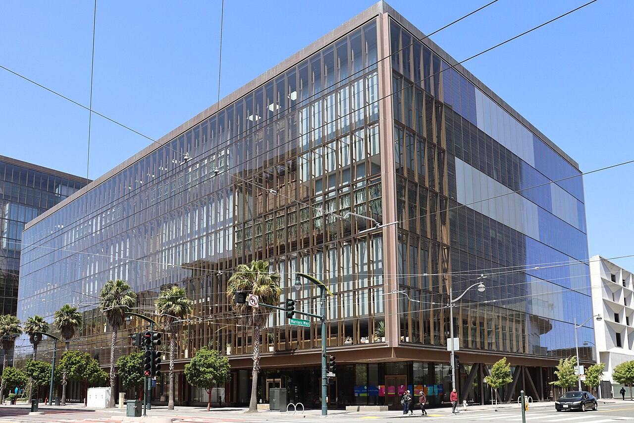 Edificio de oficinas de cristal y bronce en la esquina de Third Street con Warriors Way, en el barrio de Mission Bay de San Francisco, que era la sede de OpenAI cuando se tomó la fotografía en junio de 2025.